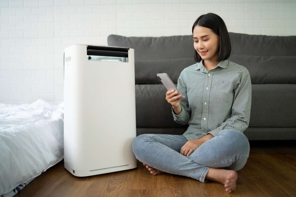Woman on her phone, sitting on the floor beside an air purifier.