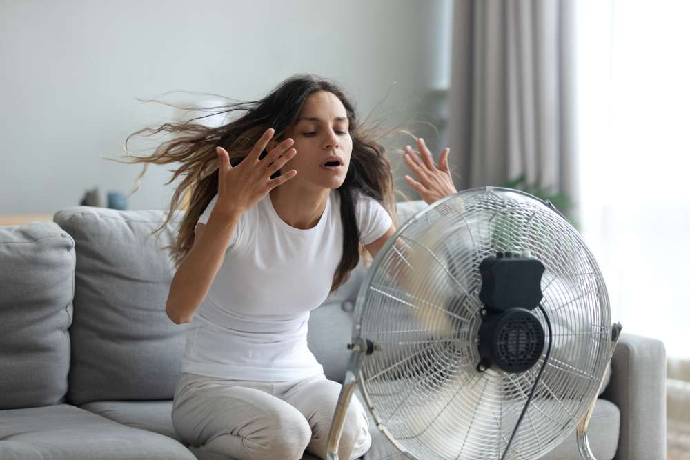 Fan blowing in a woman's face, who is trying to cool down.