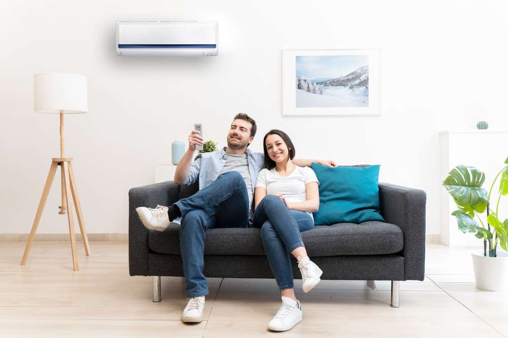 Couple sitting on a couch about to turn on an air conditioner.