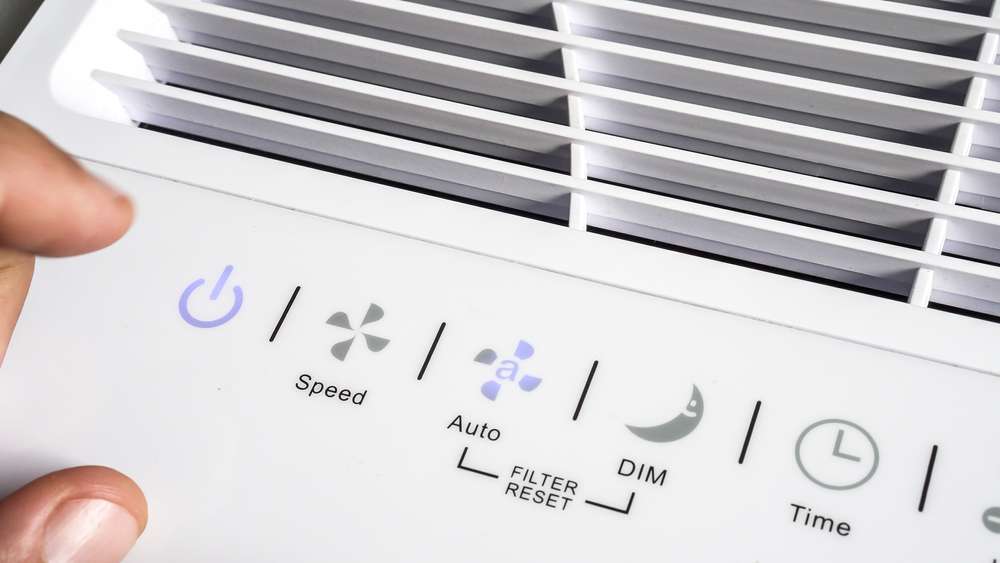 Closeup of a person's finger about to press the power button on an air purifier.