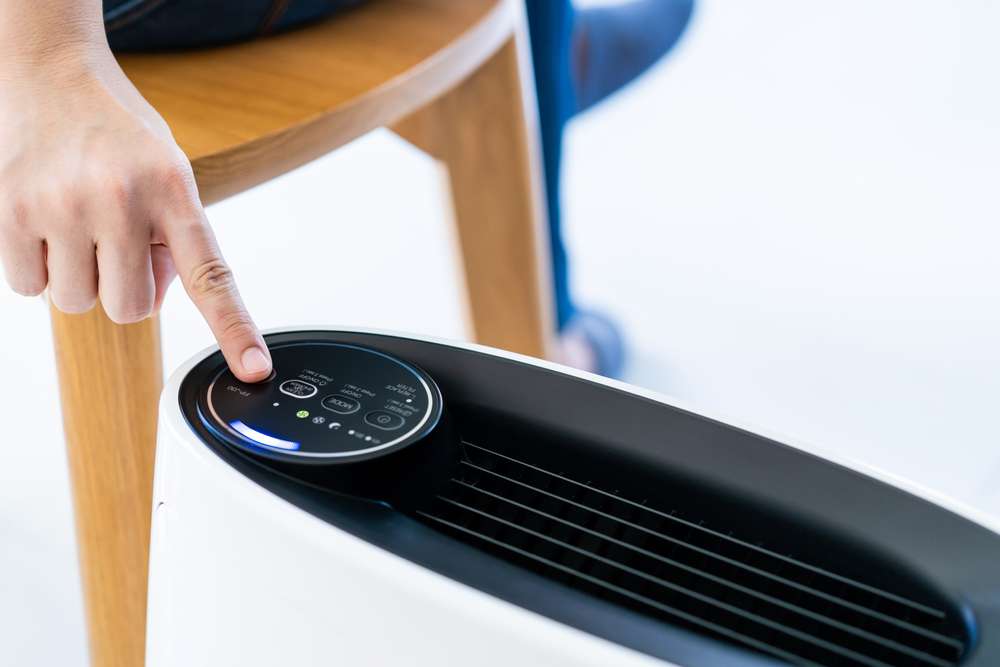 Closeup of a person's hand pushing the power button on an air purifier.