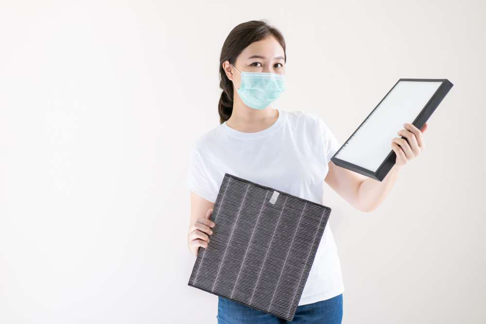 Woman with a mask on and holding an air filter in each hand.