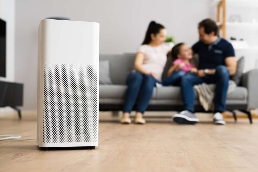 Family sitting on a couch with an air purifier in the foreground.
