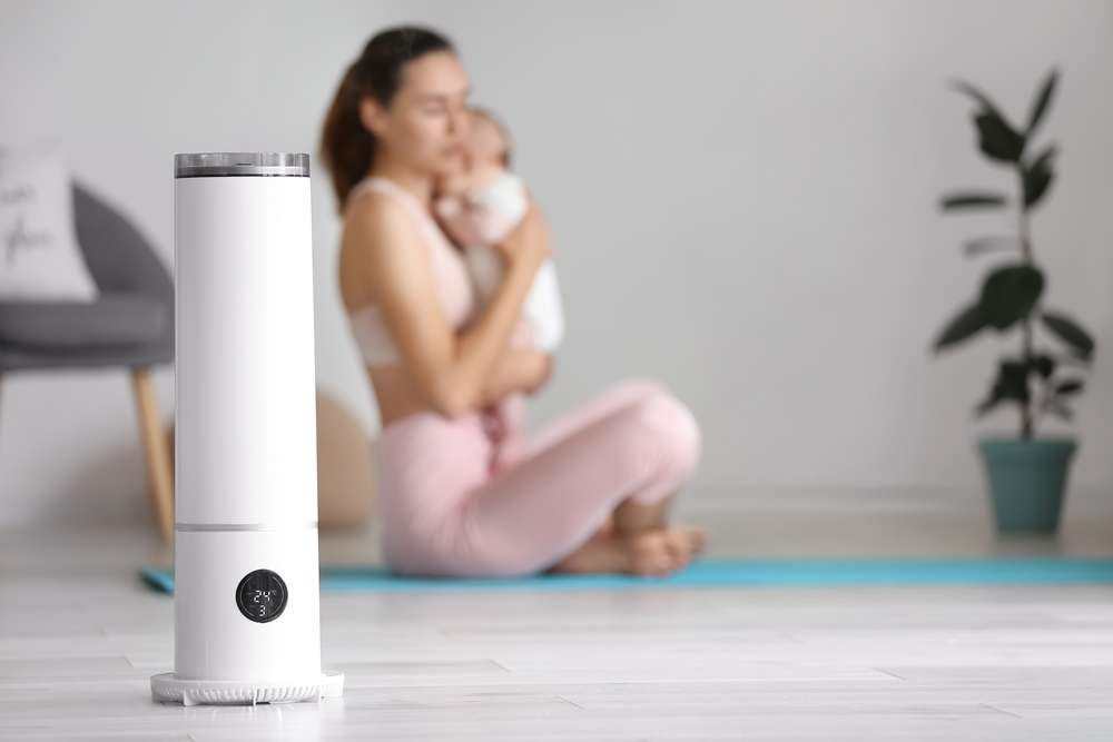 Woman holding baby in the background with an air purifier in the foreground.