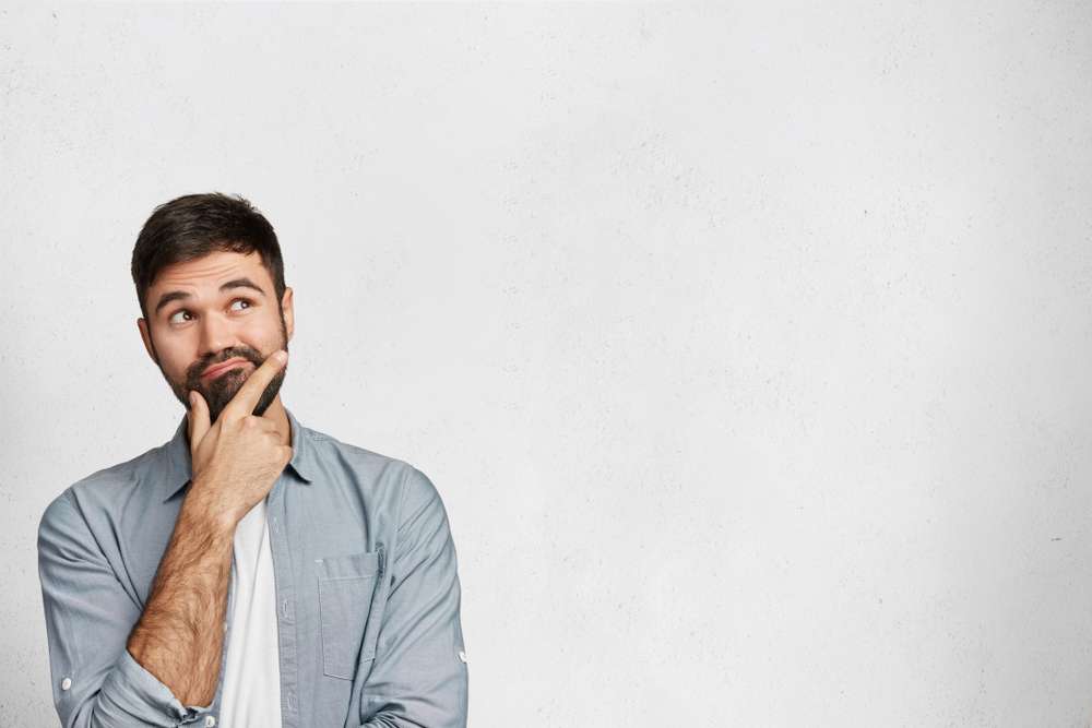 Man standing in front of a white wall, thinking.