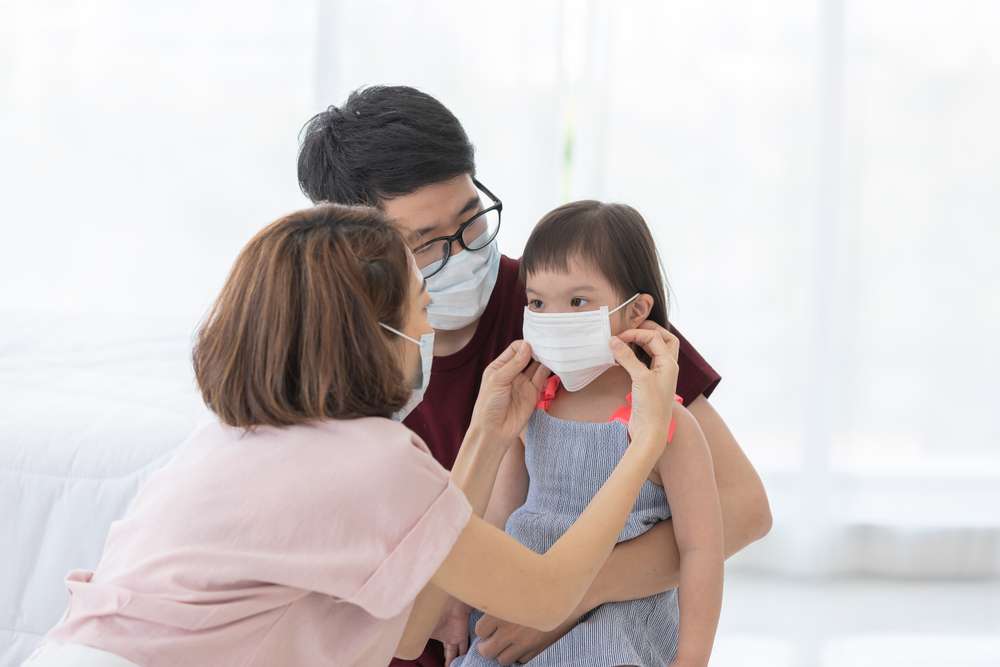Mother and father putting a mask on their daughter.